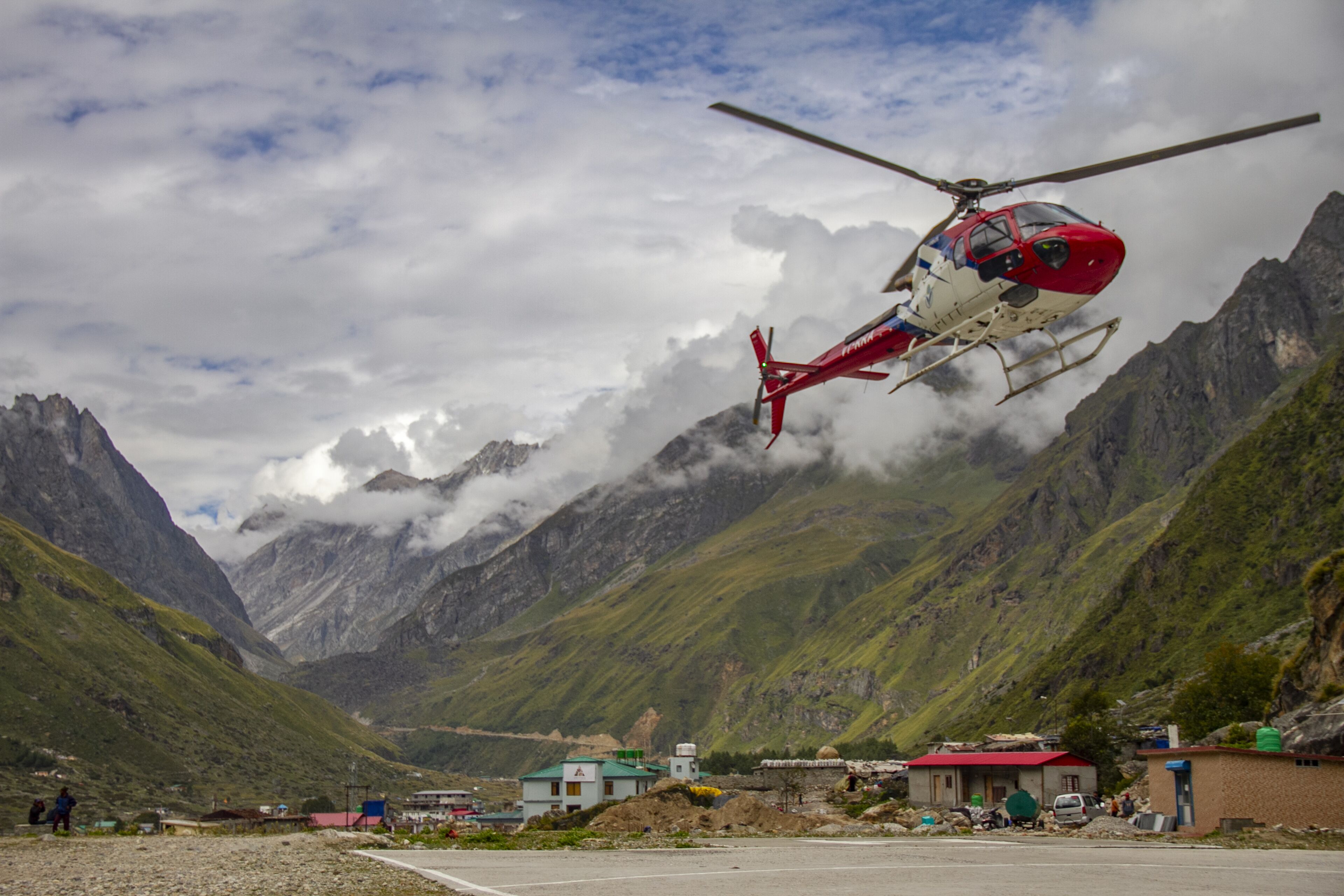 A helicopter landing on a helipad surrounded by mountains and a small settlement.