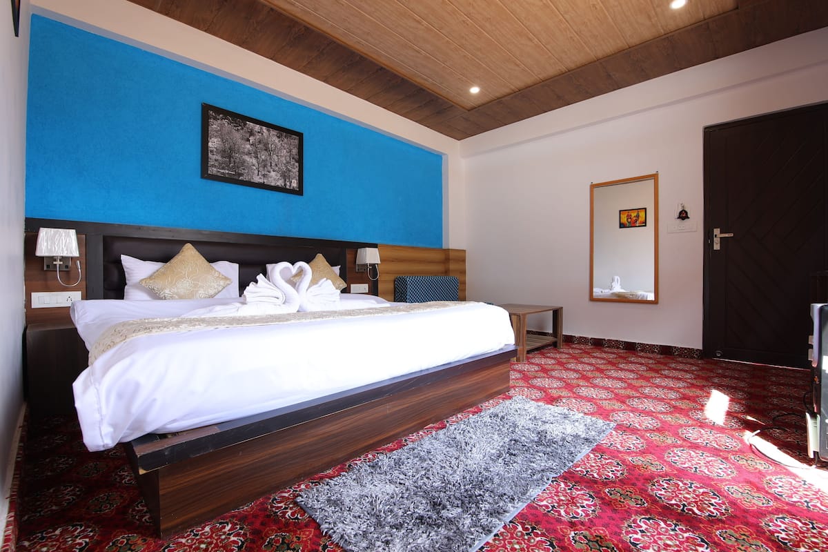 A hotel room with a large bed, a blue accent wall, a wooden ceiling, a patterned carpet, and a door.