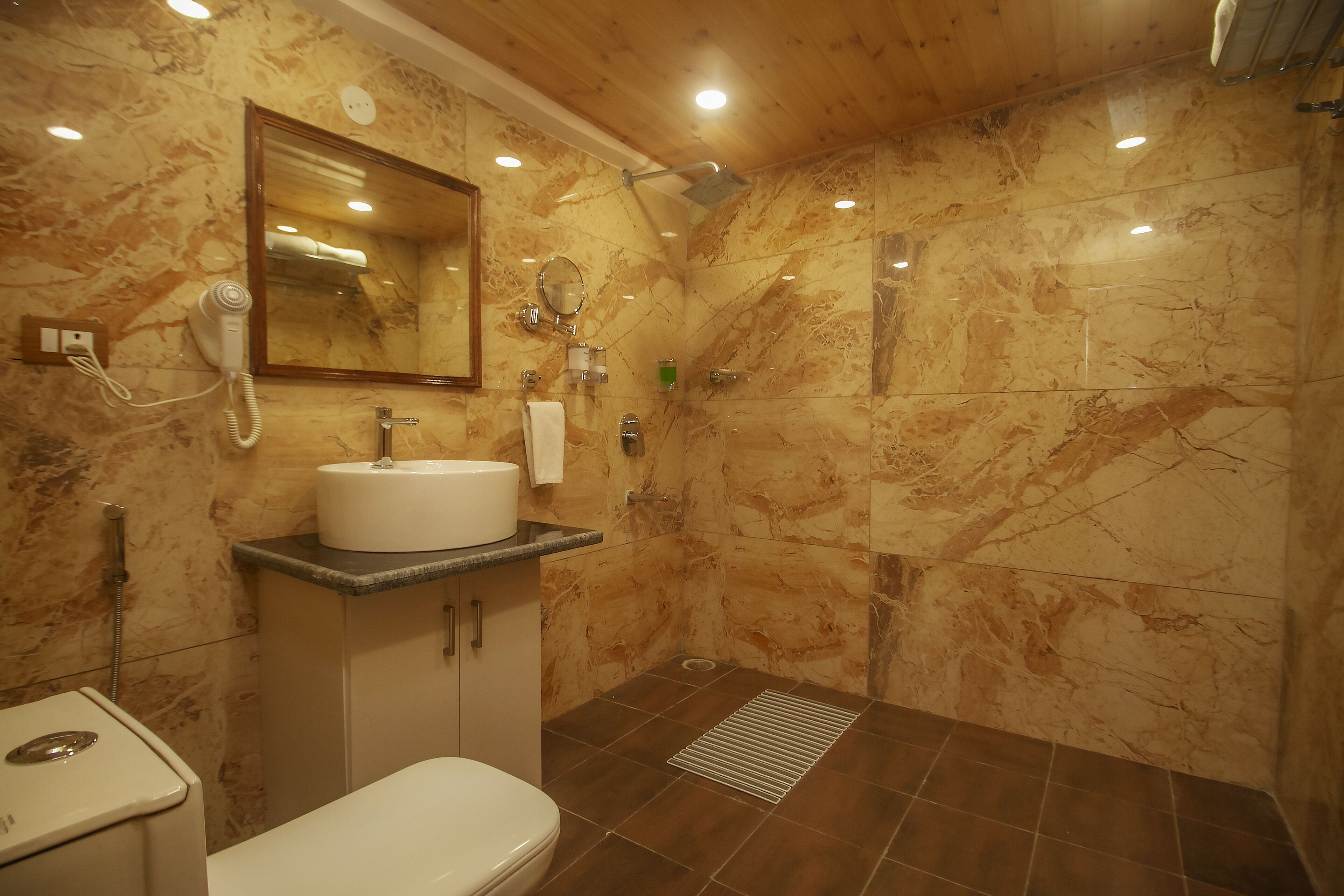A bathroom with a marble wall, a sink, a mirror, a toilet, and a shower area.