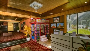 A reception area with a red carpet, a decorative kiosk, and a view of mountains through large windows. - Amritara The Avadh (Joshimath)