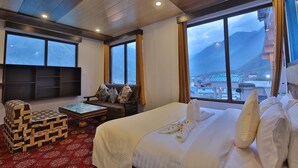 A hotel room with a large bed, a sofa, a TV, and a view of mountains. - Amritara The Avadh (Joshimath)