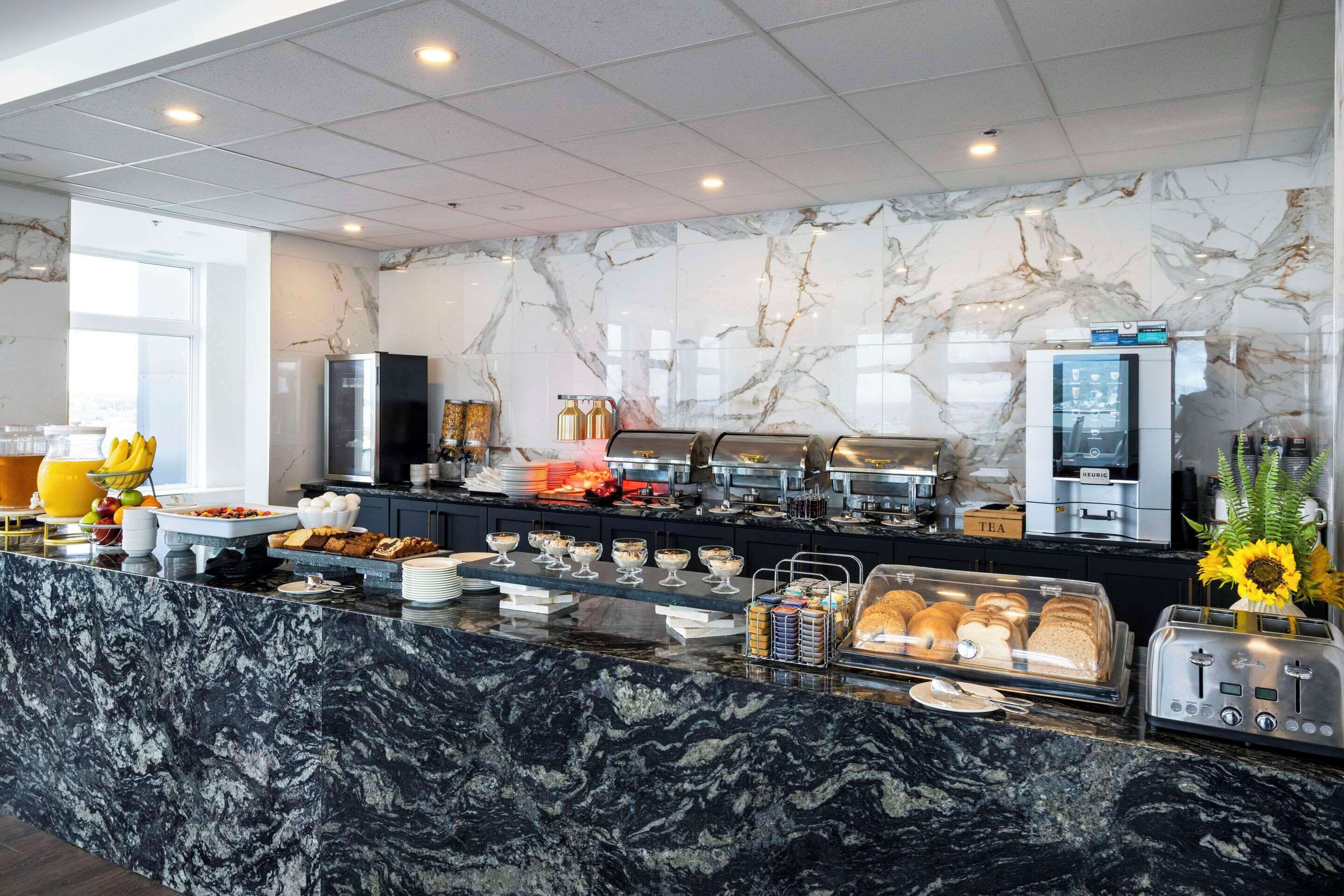 Een moderne ontbijtruimte met marmeren werkbladen, een koffieapparaat en diverse ontbijtartikelen.