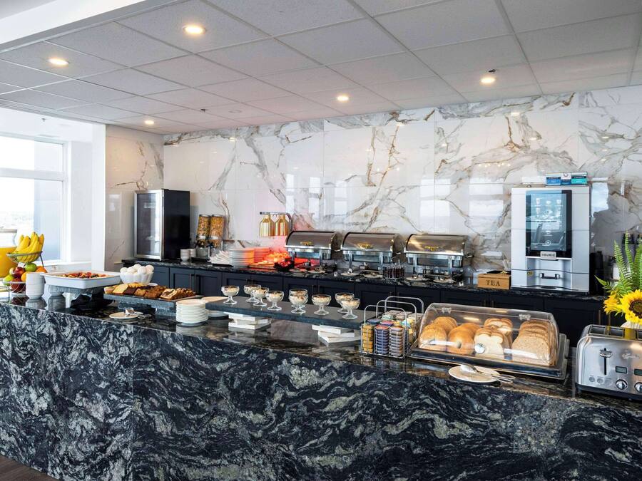Een moderne ontbijtruimte met marmeren werkbladen, een koffieapparaat en diverse ontbijtartikelen.