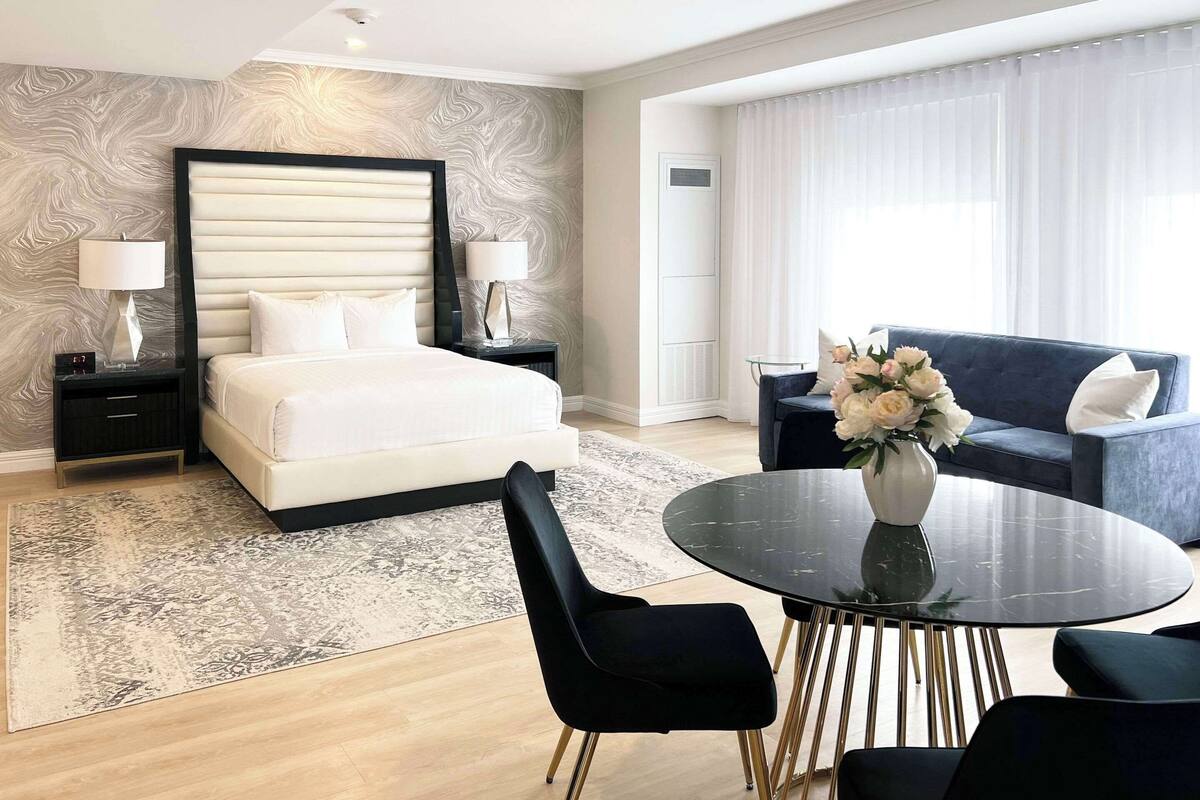 A hotel room with a large bed, bedside tables with lamps, a sofa, a round table, and a decorative vase.