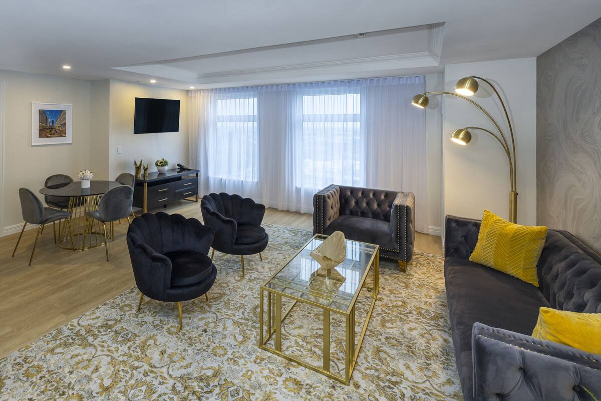 A modern living room with a sofa, armchairs, a glass coffee table, and a dining area with chairs and a table.