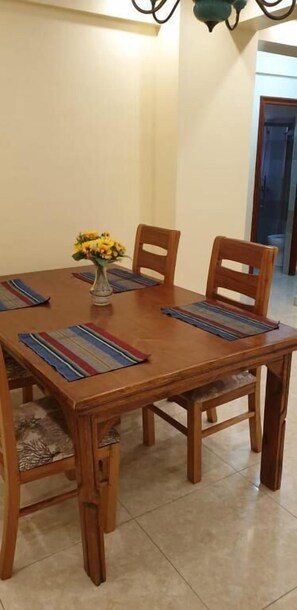 Une table de salle à manger en bois, accompagnée de quatre chaises, un vase rempli de fleurs jaunes et des sets de table à rayures.