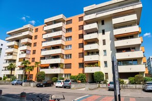 A multi-story residential building with balconies, parked cars, and a clear blue sky. - Lido Apartment Locarno With Balcony and Parking (Locarno)