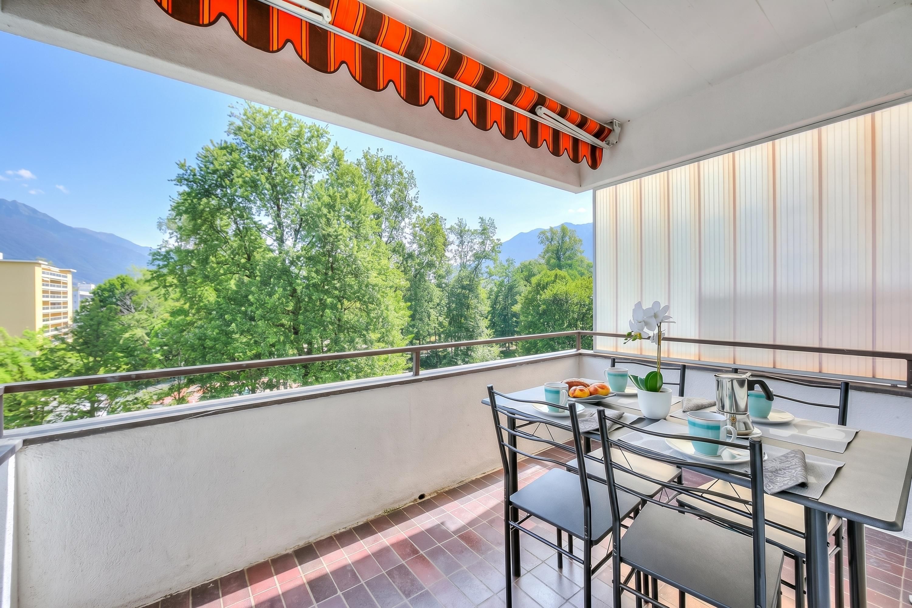 A balcony with a table, chairs, and a view of trees and mountains.
