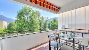 A balcony with a table, chairs, and a view of trees and mountains.