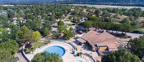 An aerial view of a resort with a large circular pool, surrounded by villas and a mountainous backdrop.
