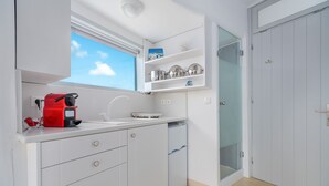 A compact kitchen with white cabinets, a red coffee maker, and a window above the sink. - Bella View Mykonos Town Suites (Mykonos)