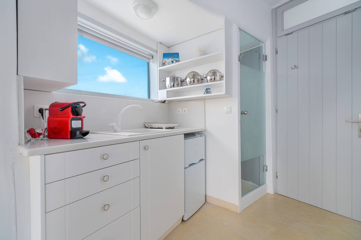 A compact kitchen with white cabinets, a red coffee maker, and a window above the sink.