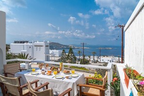 A table set for breakfast with a view of the sea and buildings in the background.