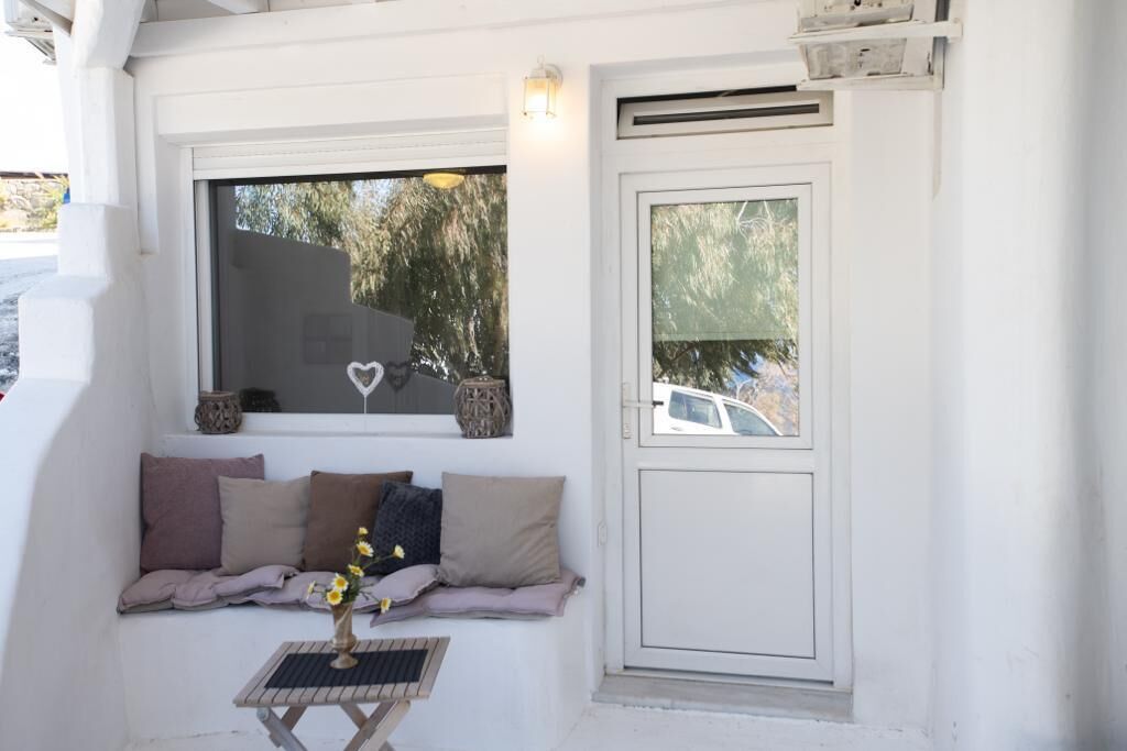 A white-walled room with a built-in bench, a small table with a vase, and a window with a heart decoration.