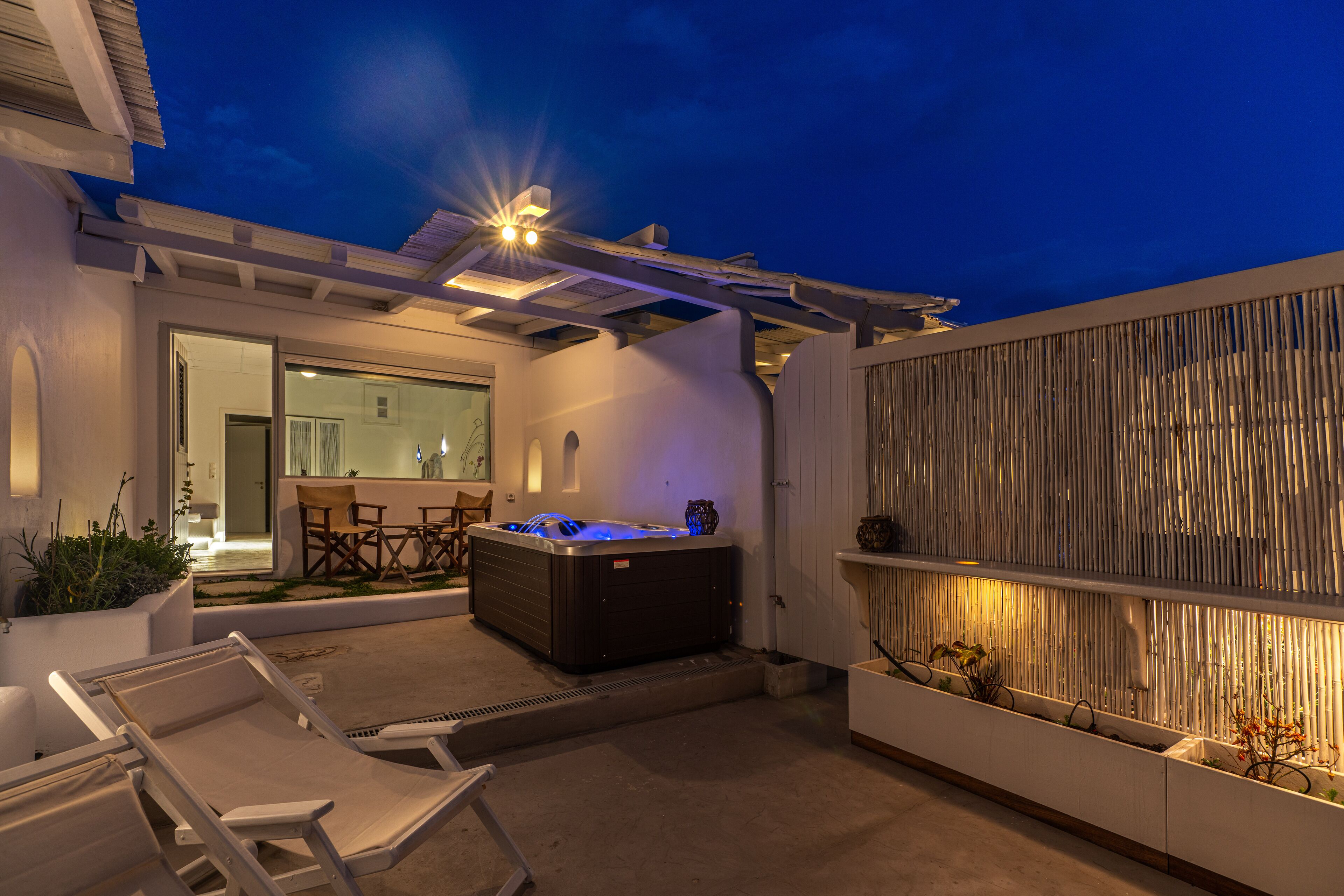 A hot tub in a covered outdoor area with lounge chairs and a wooden fence.