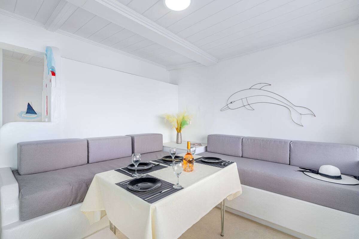 A dining area with a white table set for four, a grey sofa, and a wall-mounted dolphin artwork.