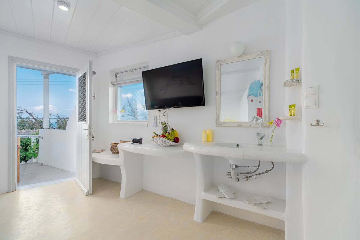 A modern bathroom with a white vanity, a mounted television, and a large mirror.