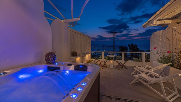 A hot tub with blue lights, white lounge chairs, and a view of the sea at dusk. - Bella View Mykonos Town Suites (Mykonos)
