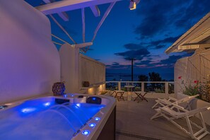 A hot tub with blue lights, white lounge chairs, and a view of the sea at dusk. - Bella View Mykonos Town Suites (Mykonos)