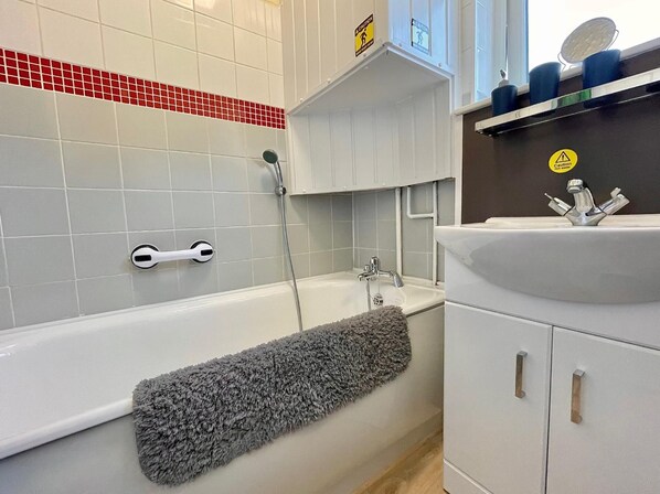 Un baño con una bañera blanca, una toalla gris, un lavamanos blanco con espejo y un salpicadero de azulejos rojos.