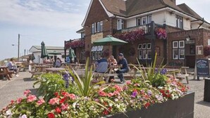 A pub with outdoor seating, a flower bed in front, and a signboard.