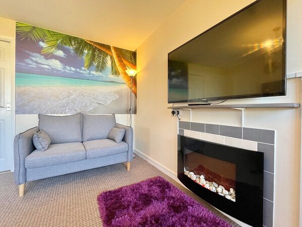 Una sala de estar con sofá, chimenea y televisor montado encima.