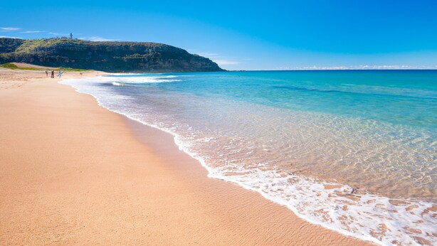 A beach with clear turquoise water, a sandy shore, and a distant hill with a structure on top.