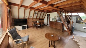 Ein rustikales Interieur mit freiliegenden Holzbalken, einem Essbereich, einem Fernseher und einer Küche.