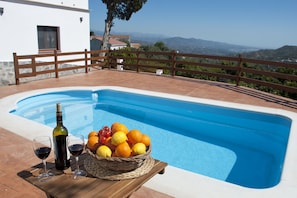 Ein Schwimmbecken mit Holzterrasse, ein Korbkorb voller Obst und zwei Gläsern Rotwein.