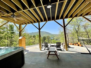 Pátio externo com hidromassagem, mesa de piquenique e cadeiras, com vista para um vale arborizado.