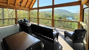 A wooden deck with outdoor furniture, large windows, and a scenic view of mountains and a lake.