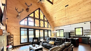 A spacious living room with leather sofas, a fireplace, and large windows offering a view of the outdoors.