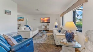 A modern living room with a white sofa, a blue sofa, and a glass coffee table. There is a painting on the wall and a lamp on a side table.