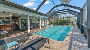 A covered outdoor swimming pool with lounge chairs and a bar area.