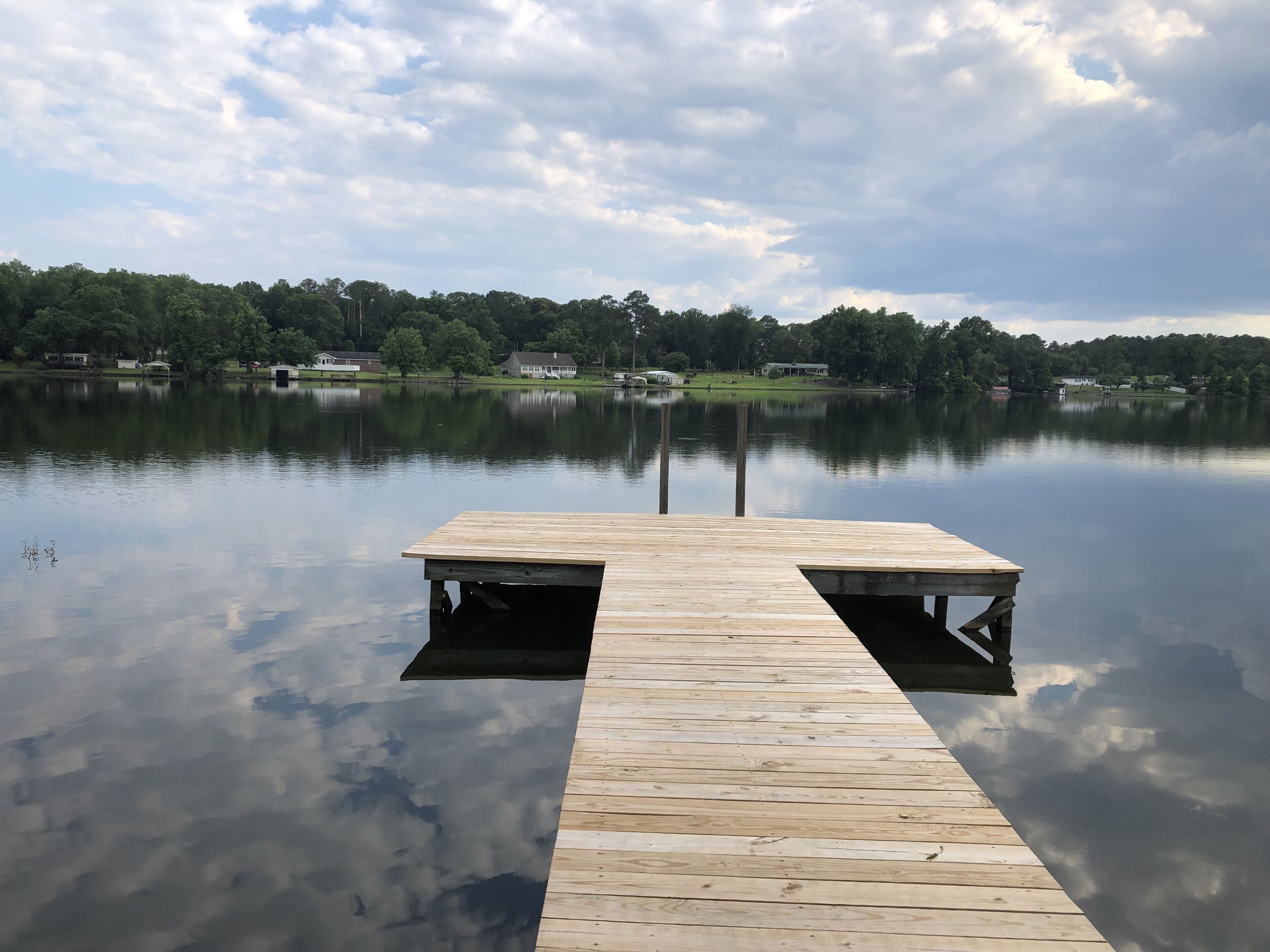 A wooden dock extending into calm water with a clear reflection of the sky and trees.