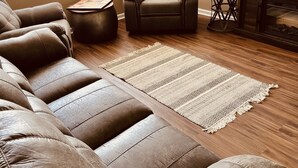 A living room with a brown leather sofa, a brown armchair, a small round table, a woven rug, and a fireplace.