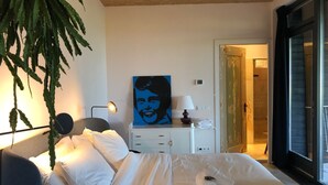 Ein Hotelzimmer mit Bett, Schreibtisch, Lampe, einem Gemälde und einer Pflanze.