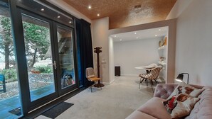 Ein modernes Wohnzimmer mit Schiebeglastür zum Garten, einem rosafarbenen Sofa und einem Essbereich mit Tisch und Stühlen.