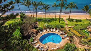 Vista aérea de un resort con piscina rodeada de sillas de descanso, palmeras y una playa.