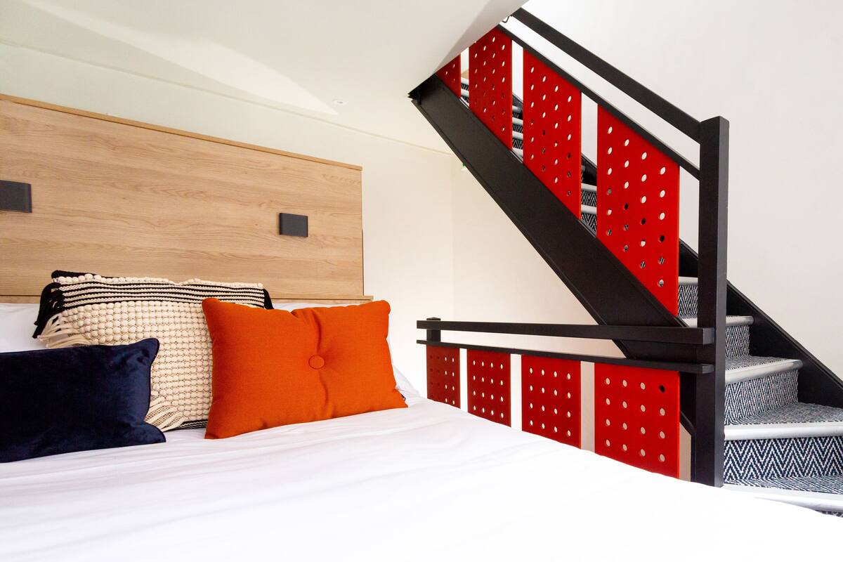 A bedroom with a bed, pillows, a headboard, and a staircase with red and black accents.