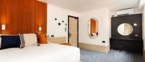 A hotel room with a bed, a wooden headboard, a mirror, a wardrobe, and a patterned floor.