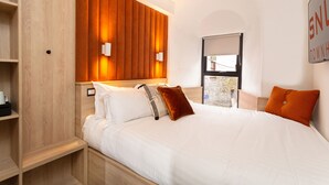 A modern hotel room with a wooden headboard, white bedding, and a view of the outside through a window. - The Snug Townhouse (Galway)