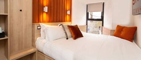 Una habitación de hotel moderna con cabecera de madera, ropa de cama blanca y vista al exterior a través de una ventana.