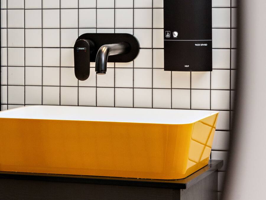 A bathroom with a white tiled wall, a black faucet, and a yellow sink.