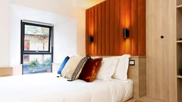 Un dormitorio moderno con cabecera de madera, cama con ropa de cama blanca, alfombra de diseño tablero de espiga y ventana con vista a un árbol de Navidad.