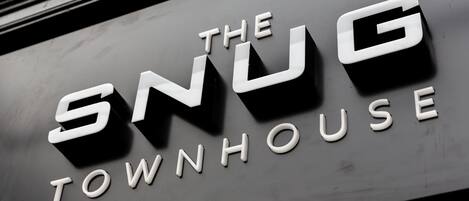 Un letrero con la inscripción 'The Snug Townhouse' en letras blancas sobre un fondo oscuro.