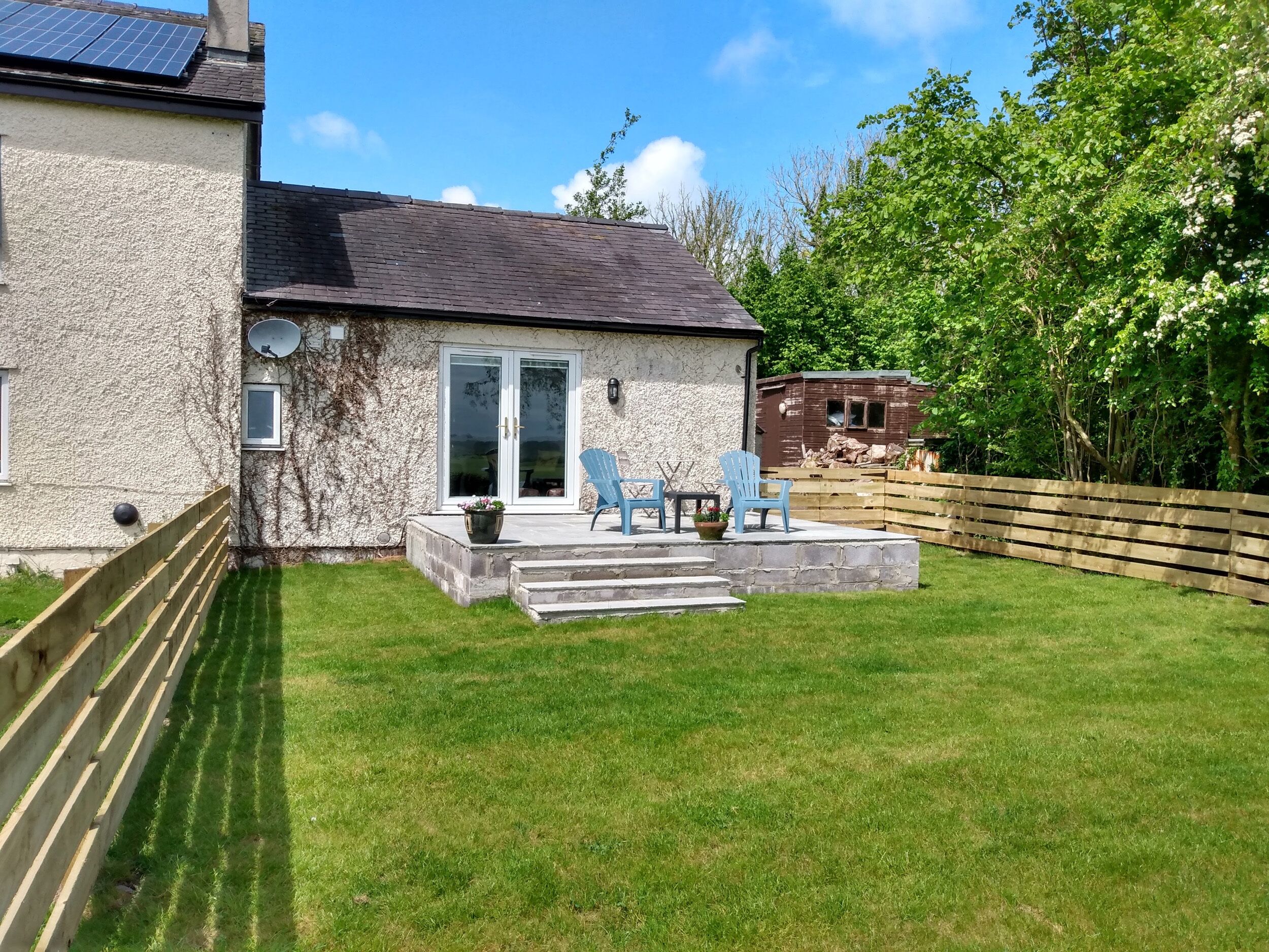 Een huis met een patio, een klein terras en een omheinde tuin.
