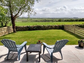 Une terrasse avec deux chaises et une table, donnant sur un champ verdoyant et un mur de pierres.