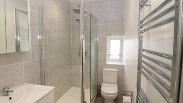 Un baño moderno con cabina de ducha de vidrio, un lavabo blanco y un inodoro.