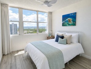 Une chambre avec un grand lit, un ventilateur de plafond, une fenêtre avec des rideaux et un tableau accroché au mur.